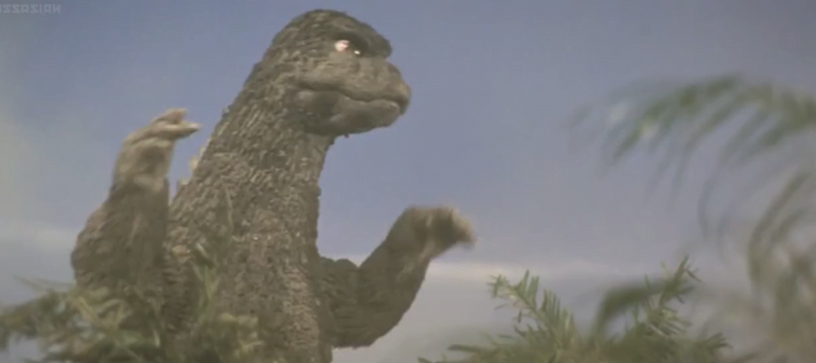 A screencap from the movie 'Godzilla vs Megalon' showing Godzilla walking to the right with a purposeful expression.