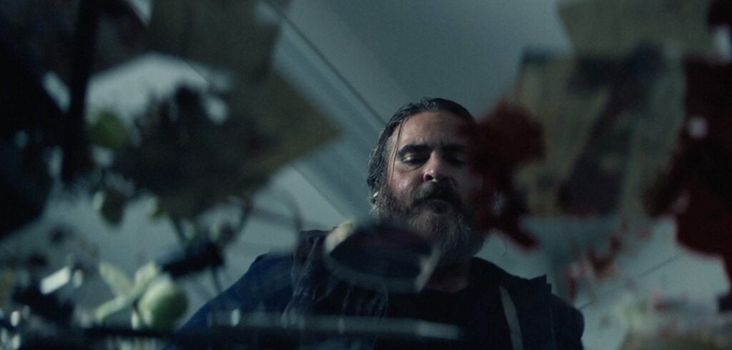 A screencap from the movie You Were Never Really Here. It shows Joe, looking down at a table covered with miscellaneous pieces but also spreading blood.